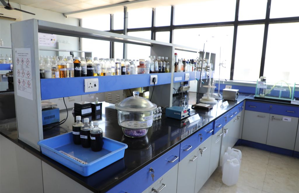Industrial lubricant testing laboratory with scientists performing quality control using chemical analysis equipment, laboratory glassware, and sample bottles in a modern R&D facility.